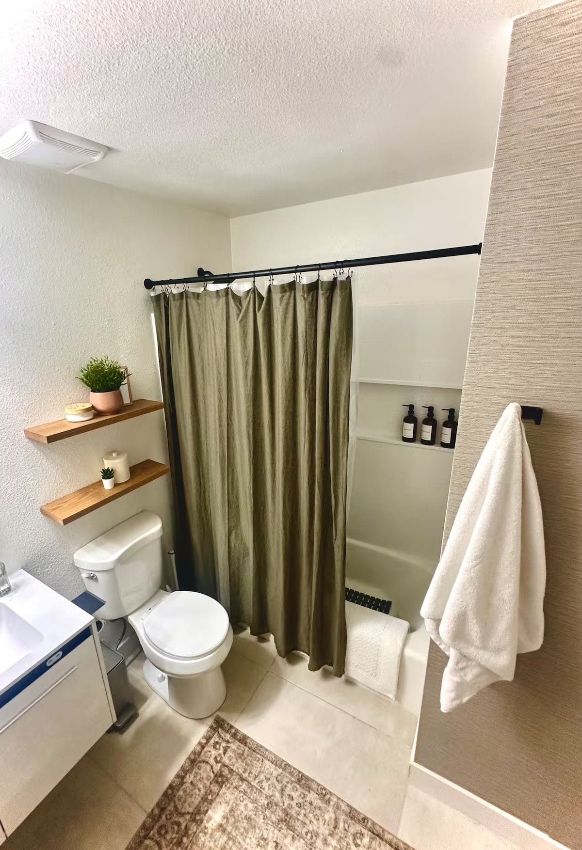 Guest bathroom after a turnover, with folded white towels hung, restocked amenities on the shelf and a scrubbed tub