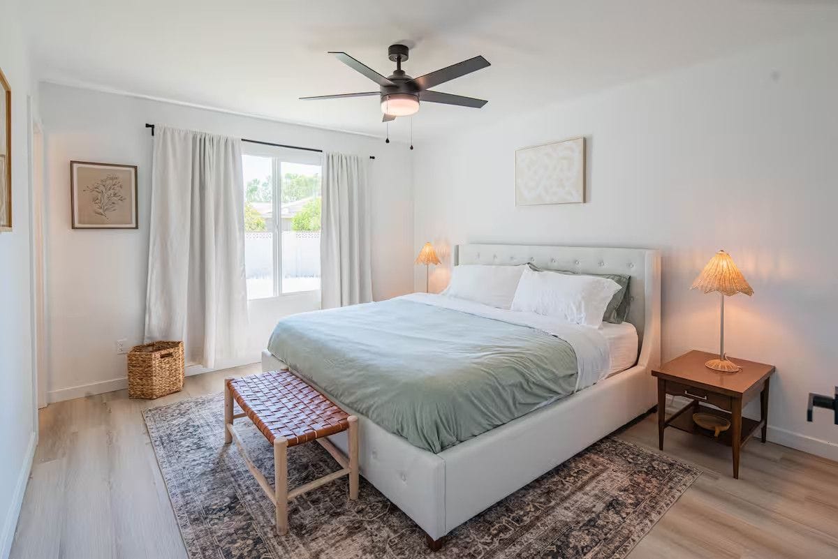 Bedroom after a turnover: king bed remade with fresh linens, dusted ceiling fan, vacuumed rug