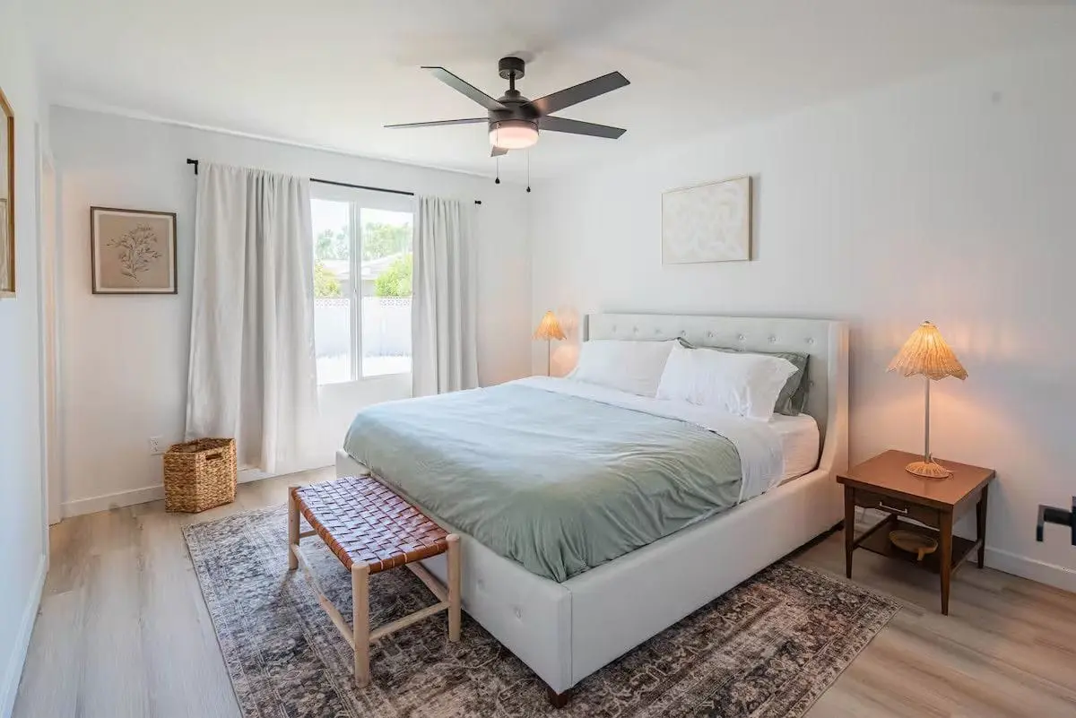 Bedroom after a turnover: king bed remade with fresh linens, dusted ceiling fan, vacuumed rug
