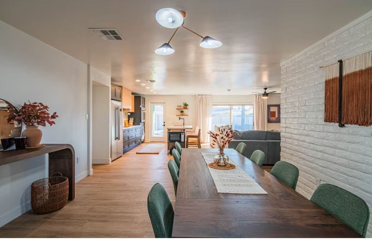 Dining table set with a runner and centerpiece, looking through to a clean open kitchen