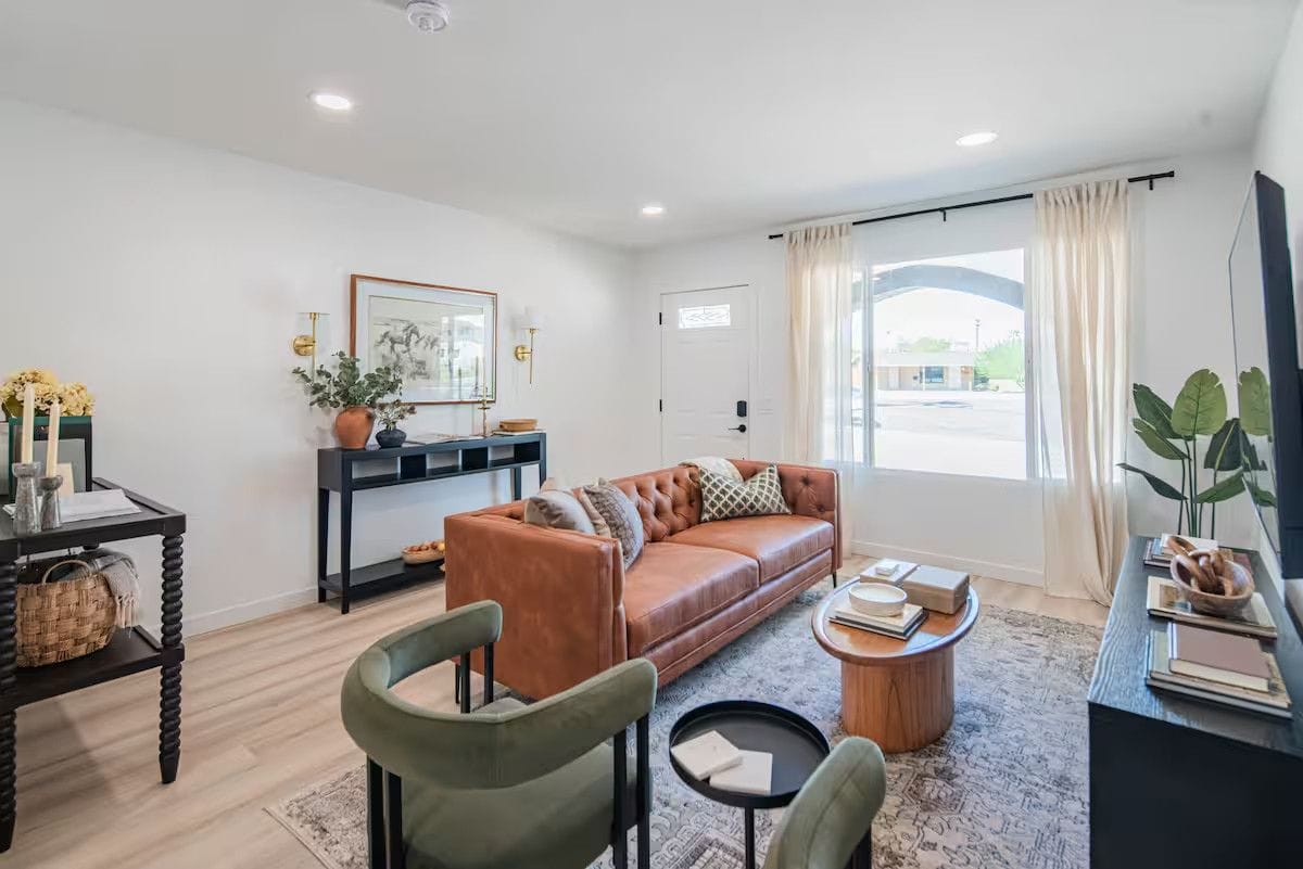 Front living room after a turnover: leather sofa with cushions squared, clean windows, vacuumed rug