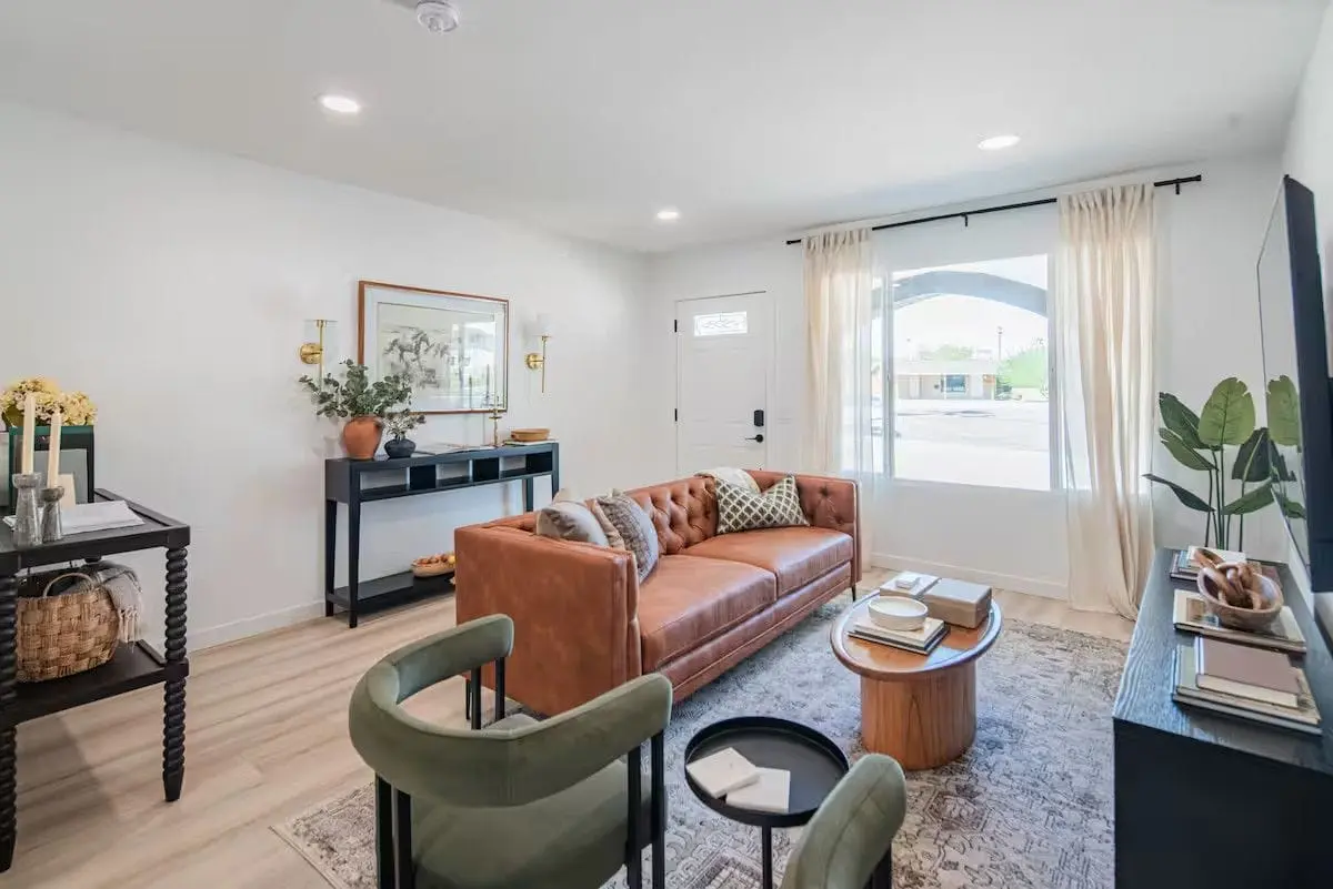Front living room after a turnover: leather sofa with cushions squared, clean windows, vacuumed rug