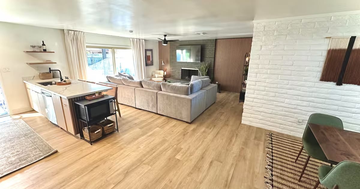 Open-plan living room after a turnover: sectional staged with cushions, clear floors, kitchen island wiped down
