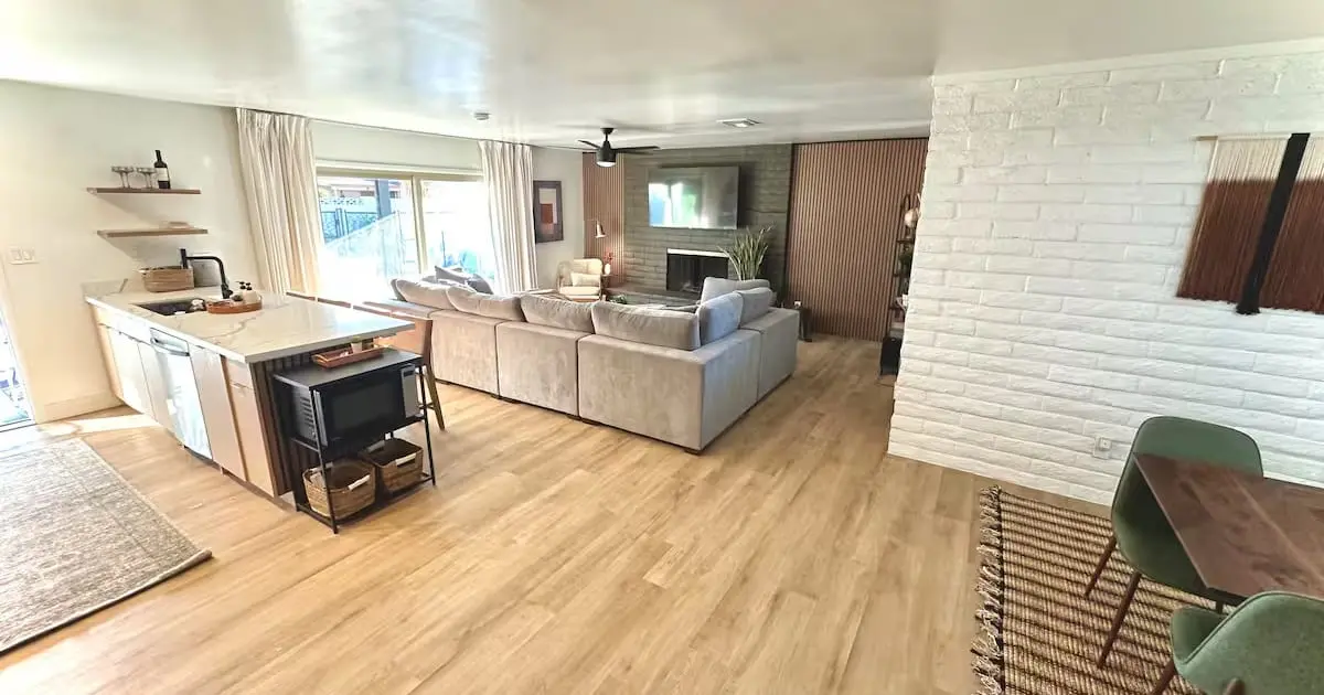 Open-plan living room after a turnover: sectional staged with cushions, clear floors, kitchen island wiped down